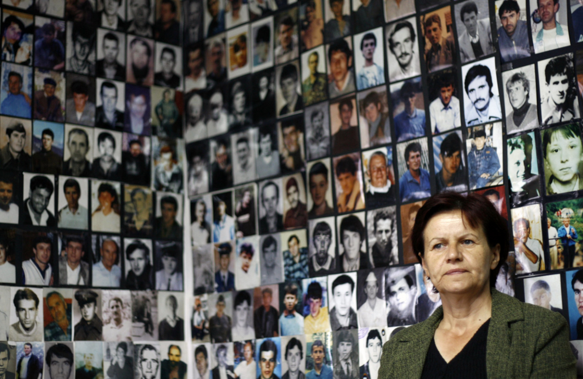 Босанка од Сребреница седи под сликите на жртвите на масакрот во градот и го гледа преносот од судењето на Ратко Младиќ.