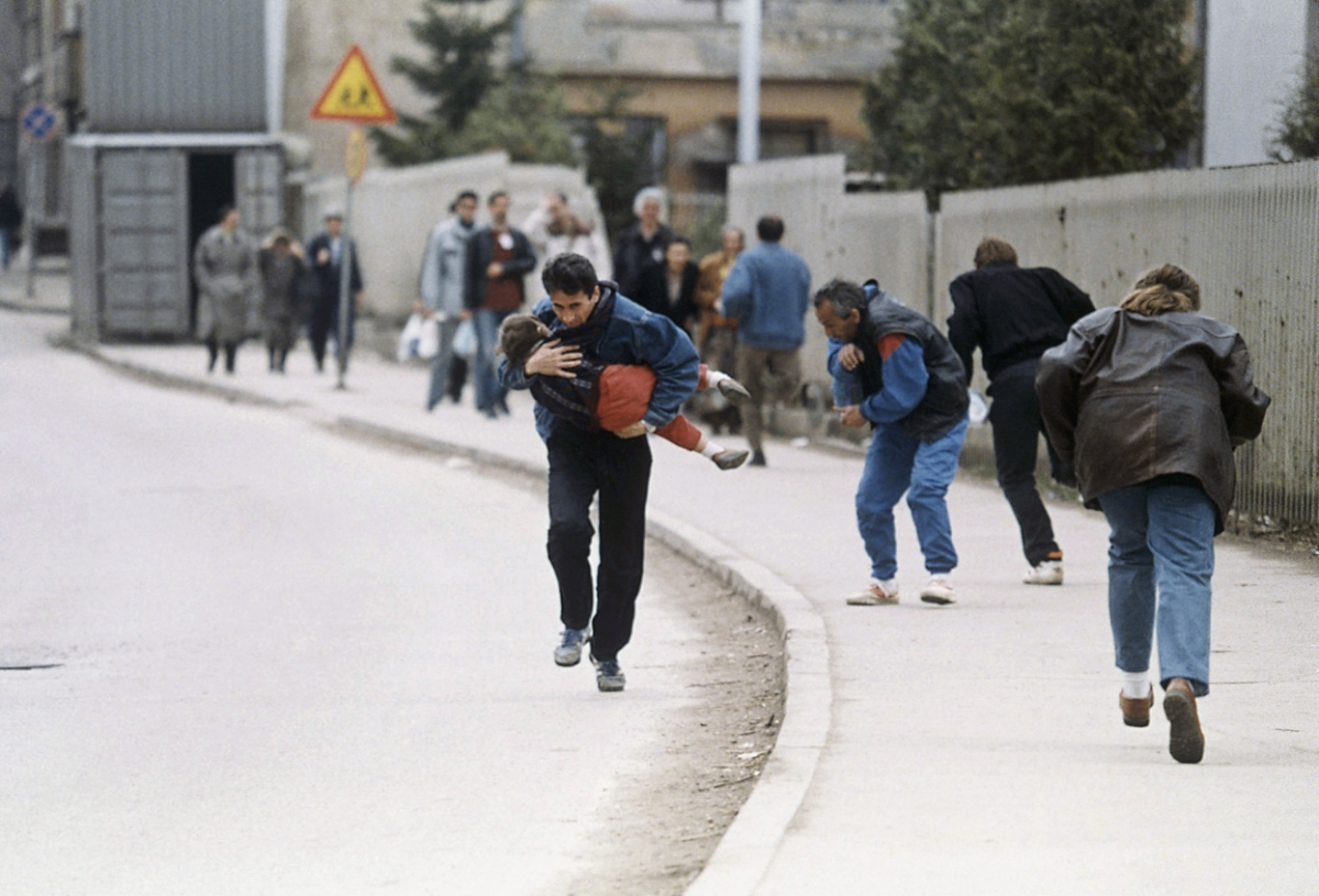 Татко го заштитува своето дете, додека трчаат преку една од најопасните снајперски точки за пешаците во Сараево. 11-ти април 1993.
